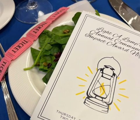 Light A Lamp Community Impact Awards program lying on a salad plate, with raffle tickets across edge of plate